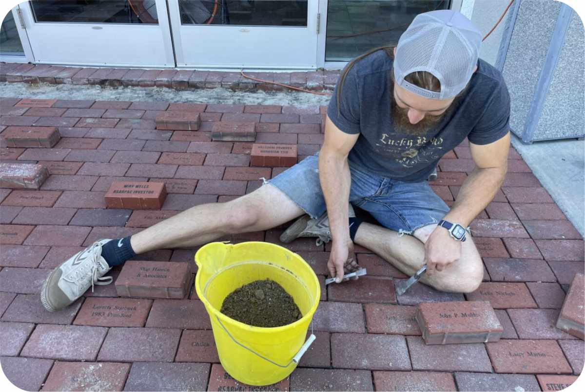 Person laying engraved bricks on sidewalk